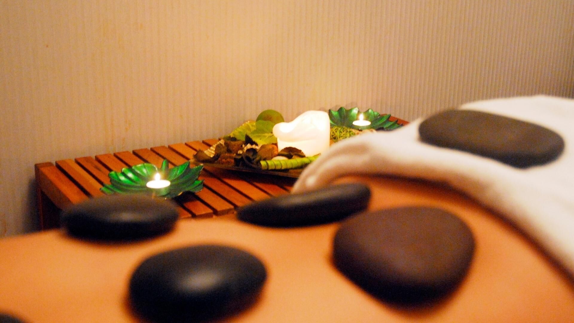 Mesa de masaje con piedras negras y una vela.