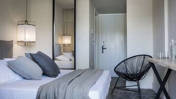 A modern hotel room with a large bed, a chair, a desk, and a mirror.