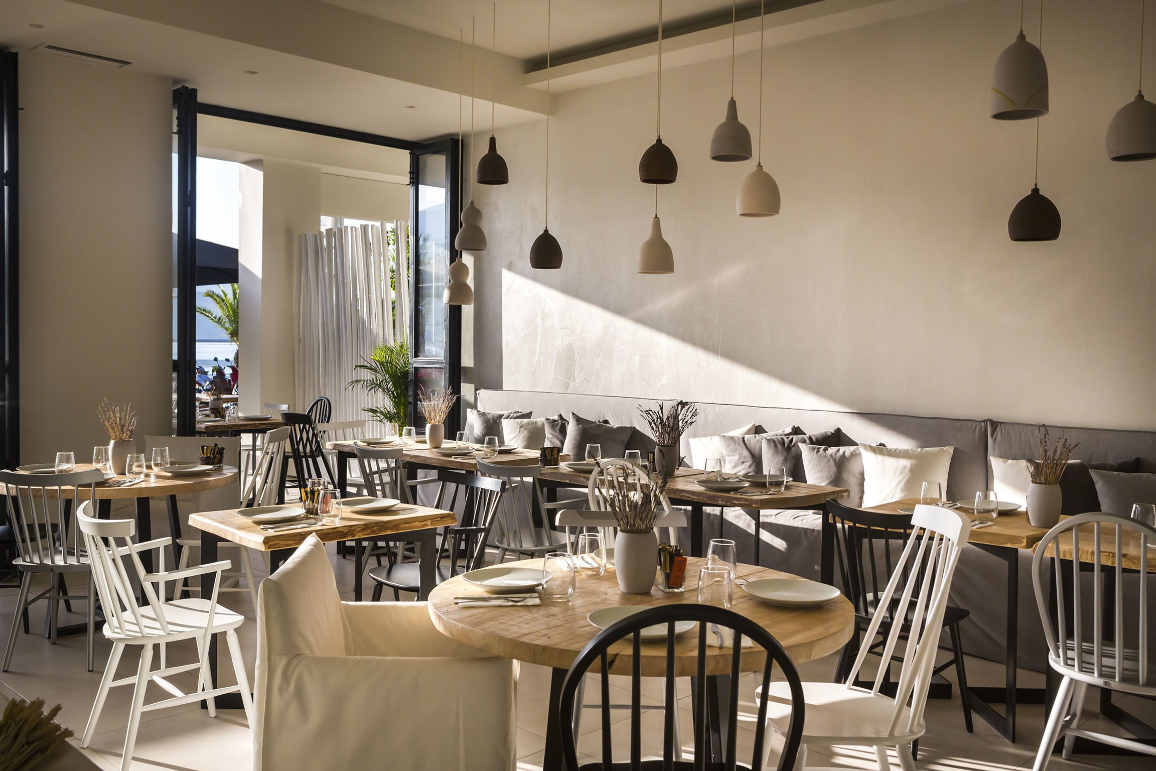 A modern dining area with multiple tables and chairs, some with white cushions.