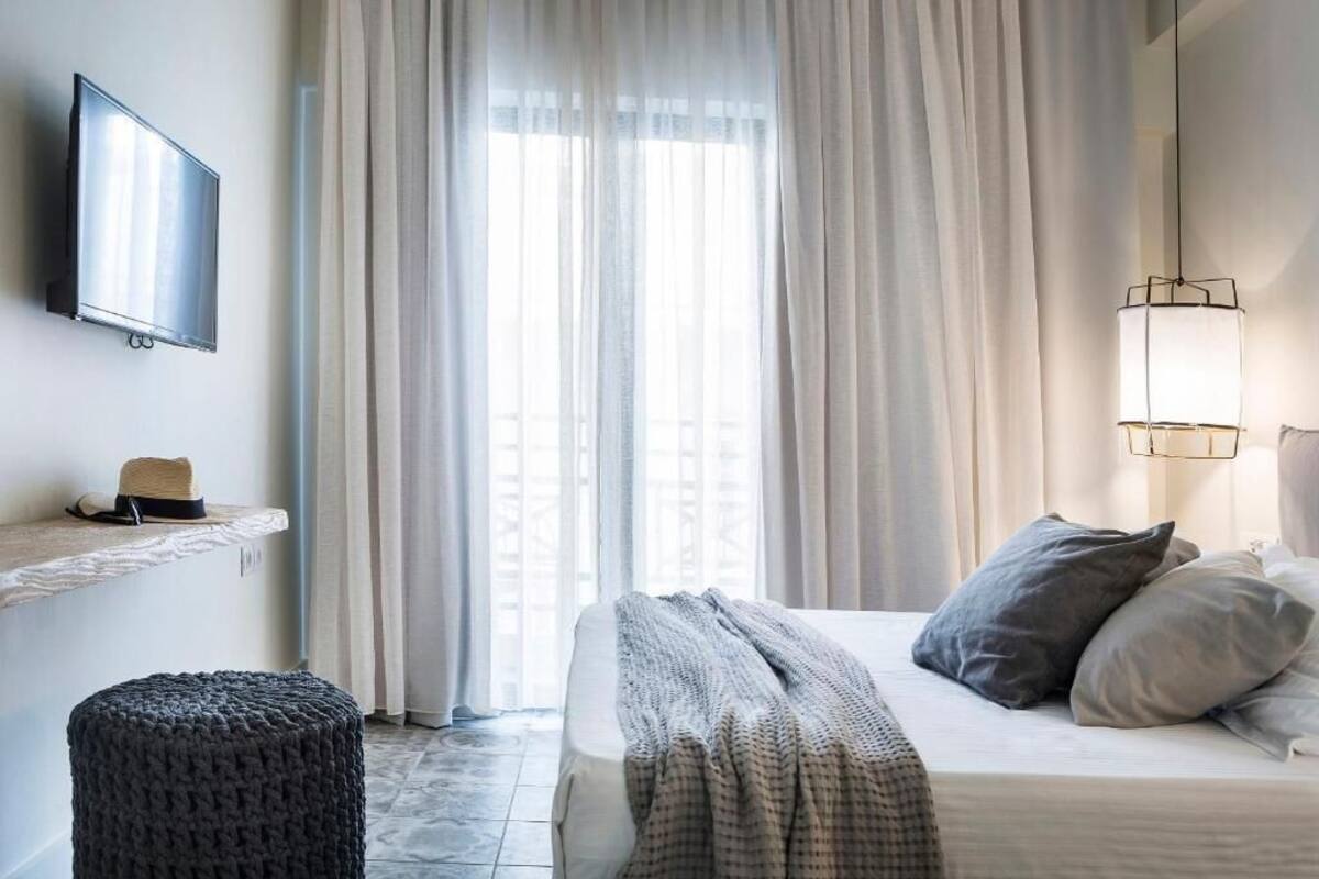 A bedroom with a bed, a television on the wall, a shelf with a hat, and a window with curtains.