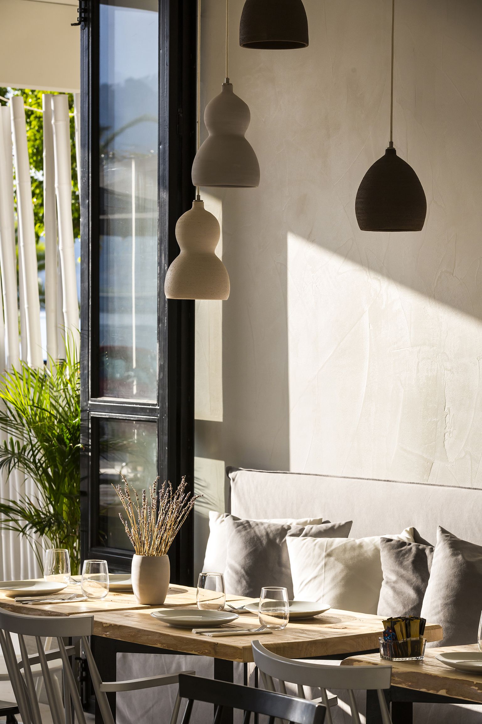 Comedor con mesa de madera para dos personas, una planta en maceta y lámparas colgantes.