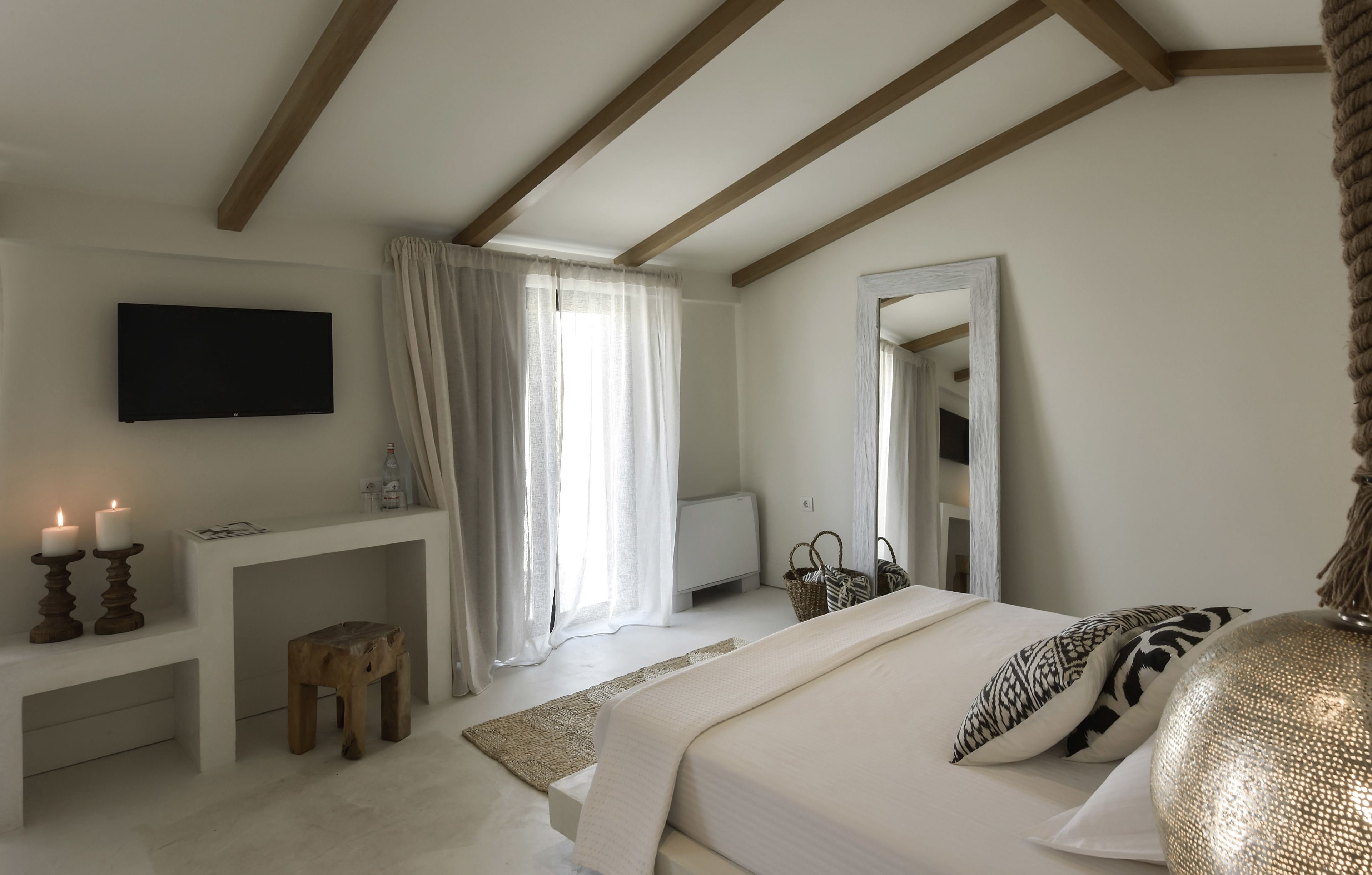 A bedroom with a bed, bedside table, TV, and a window with curtains.