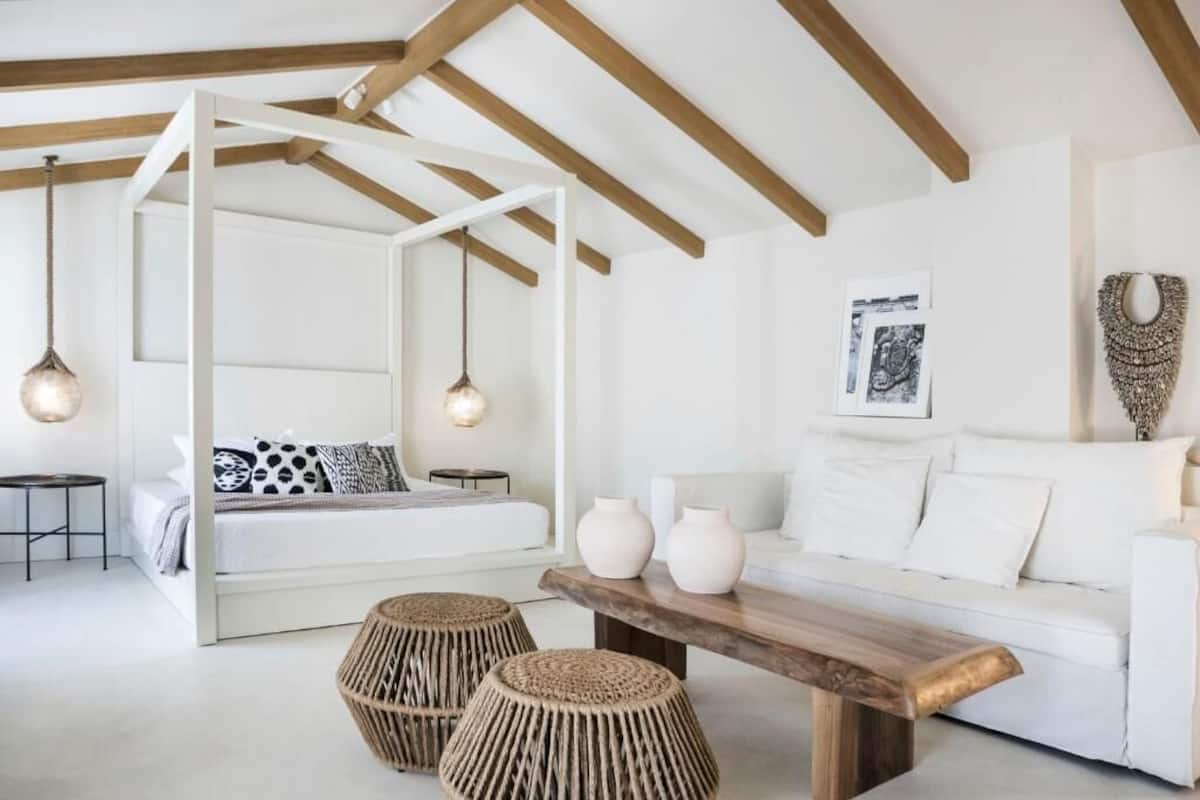 A modern bedroom with a white canopy bed, a white sofa, and a wooden coffee table.