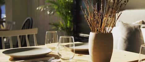 A dining table with a vase of dried plants, empty plates, and glasses.