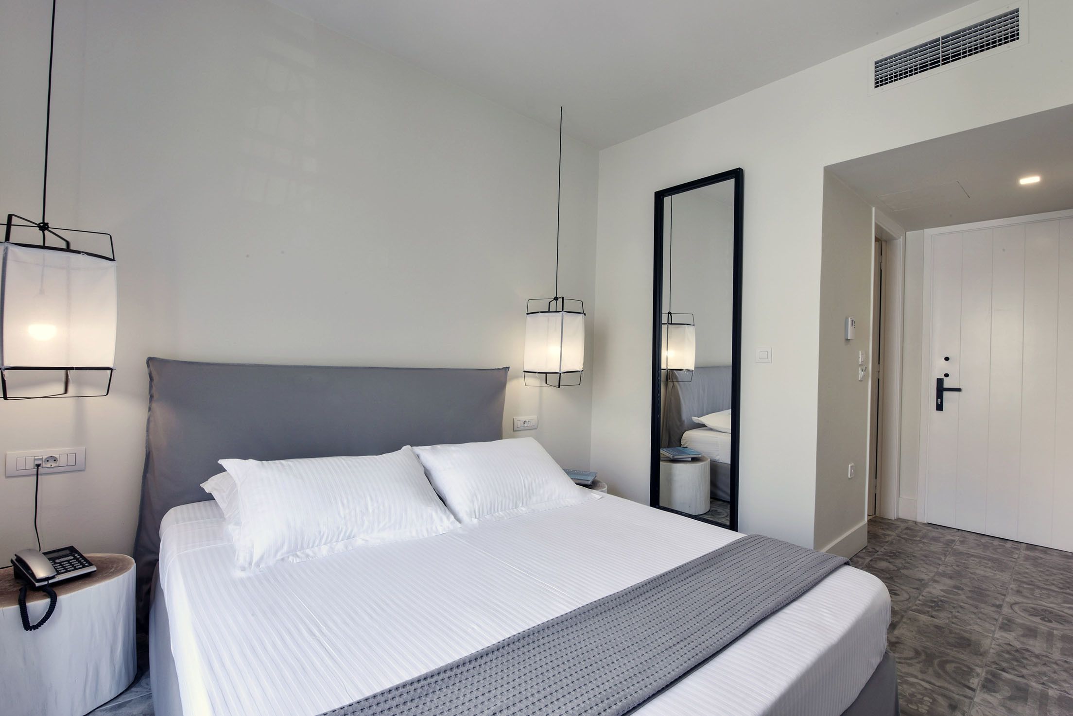 Ein modernes Hotelzimmer mit einem großen Bett, Nachttischlampen, einem Spiegel und einer Tür zu einem Badezimmer.