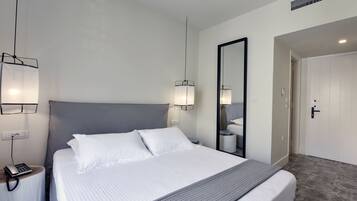 Una habitación de hotel moderna con una cama grande, lámparas de noche, un espejo y una puerta que da a un baño.