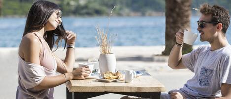 A couple sitting at a table with a view of the sea and mountains.