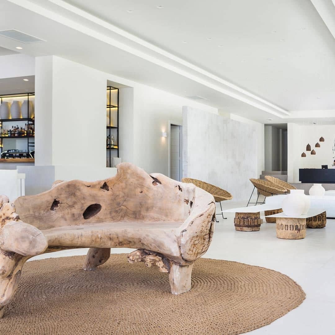 A modern living room with a unique wooden bench, a bar area in the background, and a minimalist design.