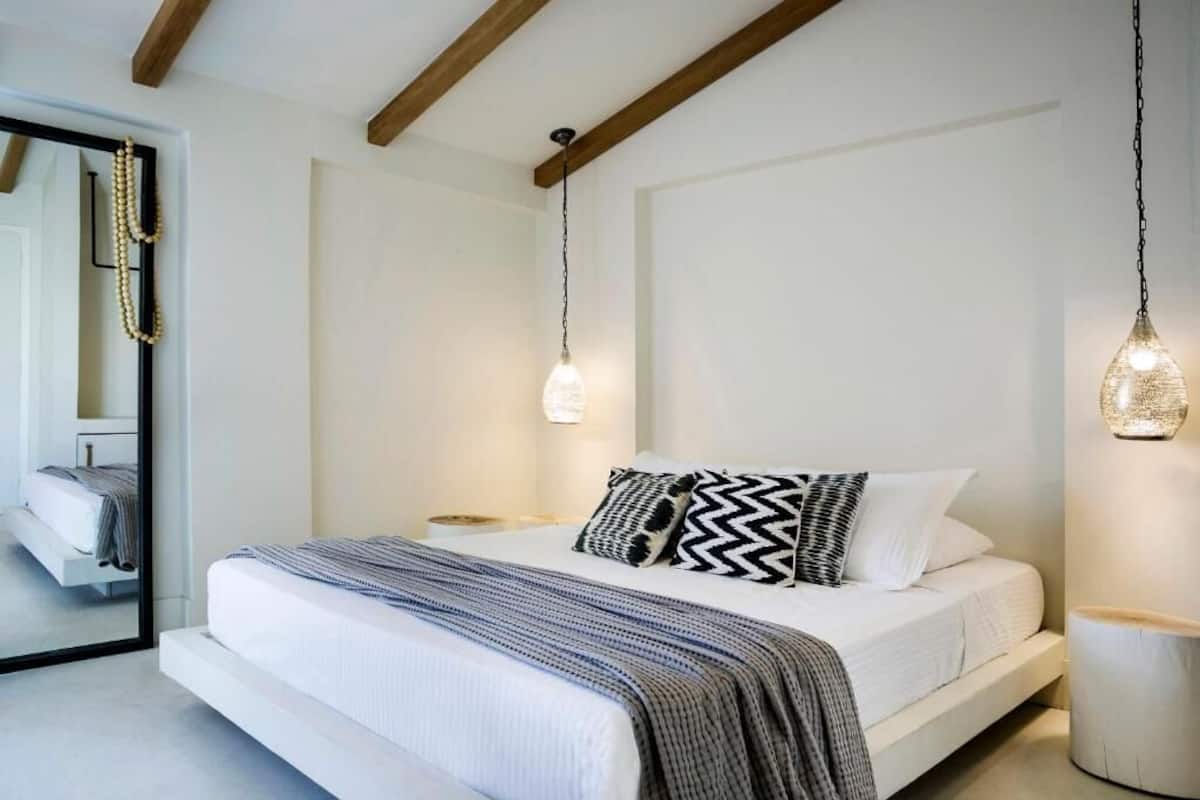 A modern bedroom with a bed, bedside tables, and hanging pendant lights.