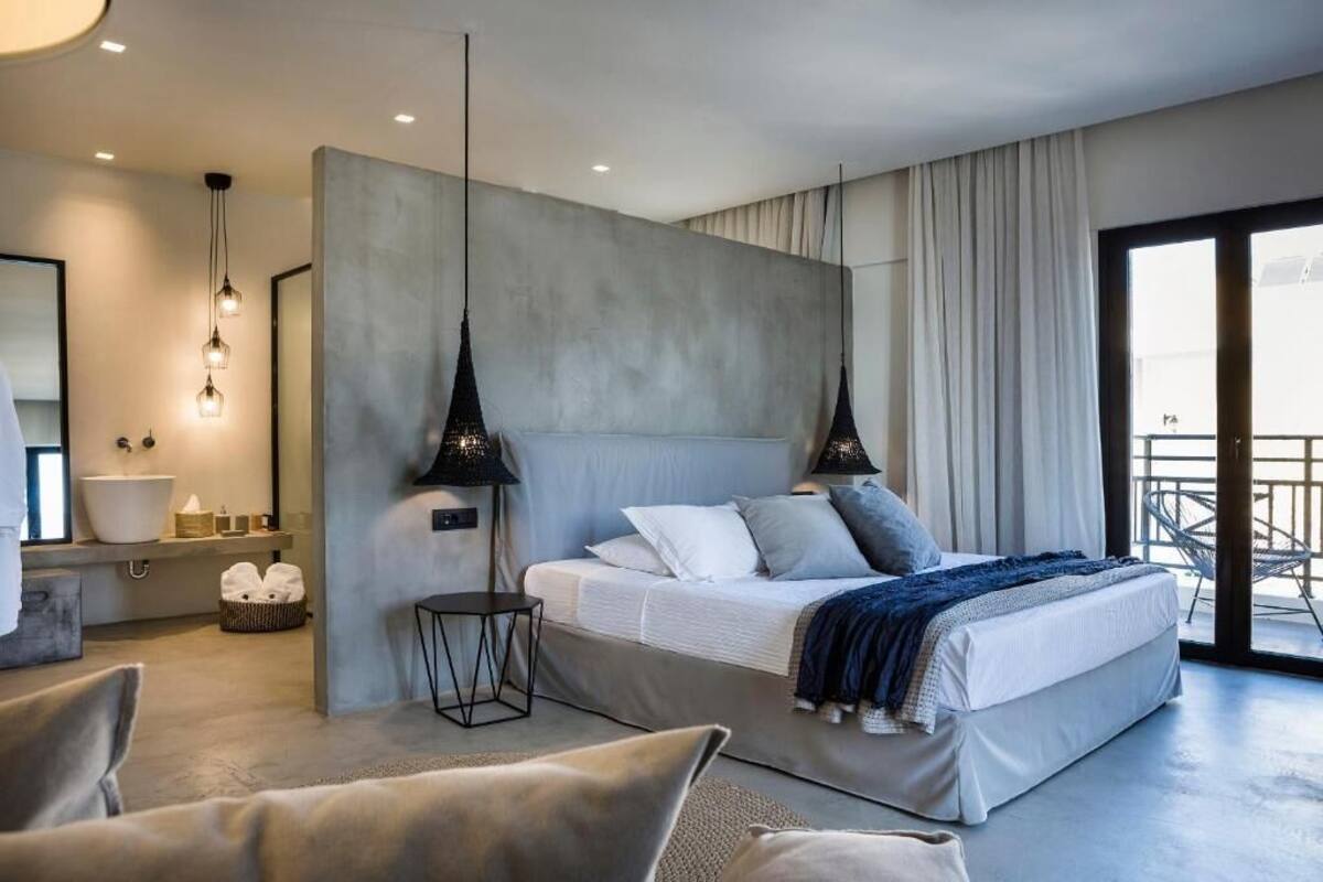 A modern bedroom with a large bed, bedside tables, a small side table, and a view of the balcony.