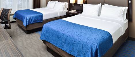 Habitación de hotel con dos camas, cada una con colcha azul estampada, una mesita de noche con lámpara y una silla.