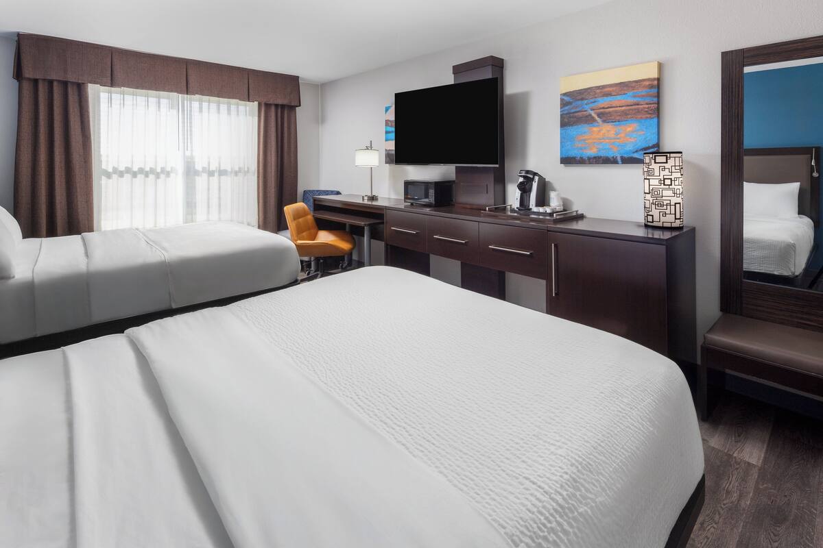 A hotel room with two beds, a desk, a chair, a television, a coffee maker, and artwork on the walls.