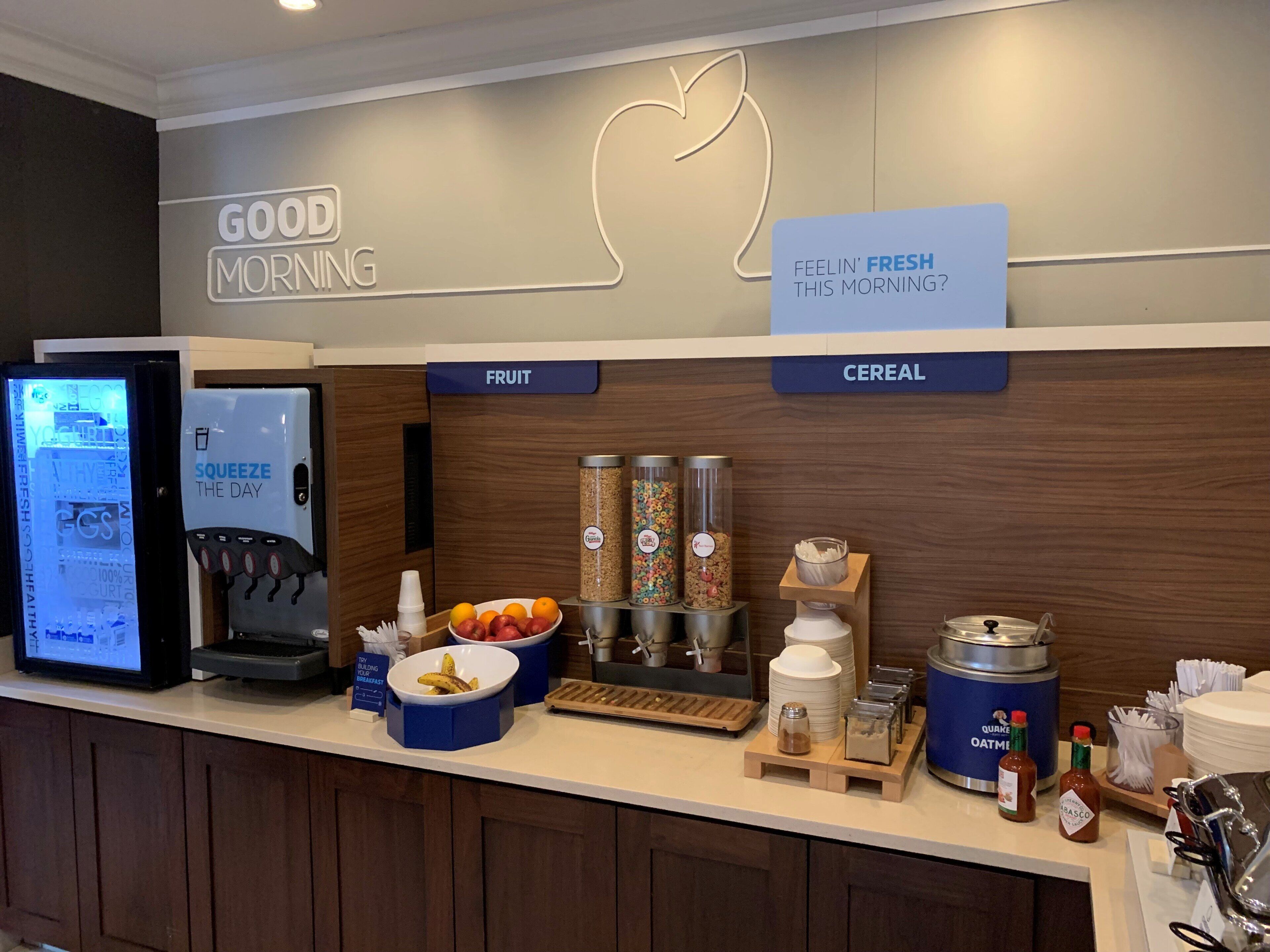 Un comptoir pour le petit-déjeuner équipé d’un écran numérique affichant le menu, de présentoirs à fruits, de distributeurs de céréales et de condiments.