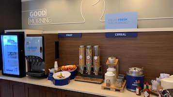 Un comptoir pour le petit-déjeuner équipé d’un écran numérique affichant le menu, de présentoirs à fruits, de distributeurs de céréales et de condiments.