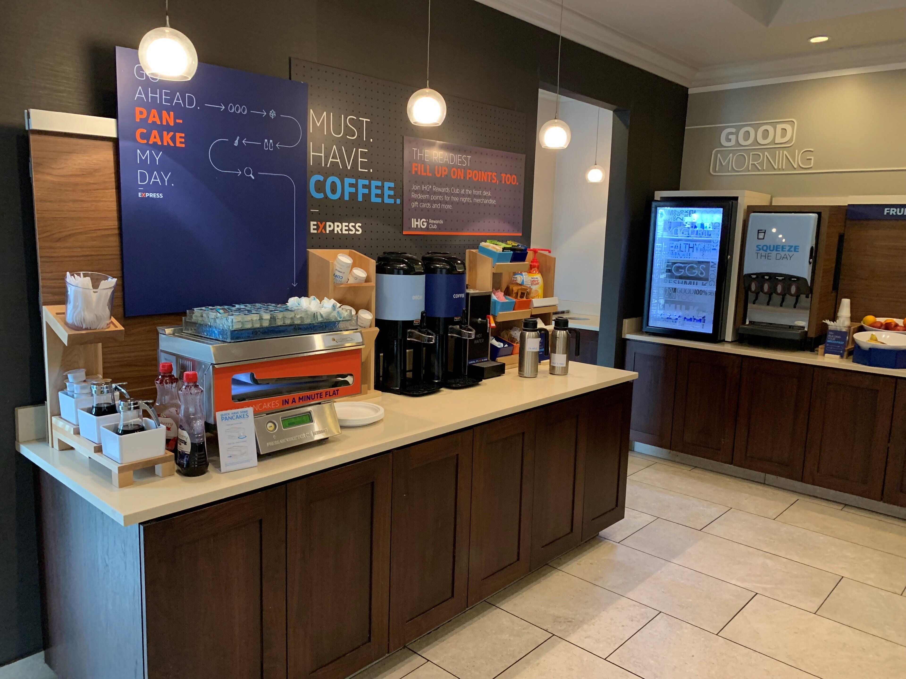 Un comptoir de café avec une machine à café, une pancarte indiquant « BONJOUR » et un écran numérique affichant un menu.