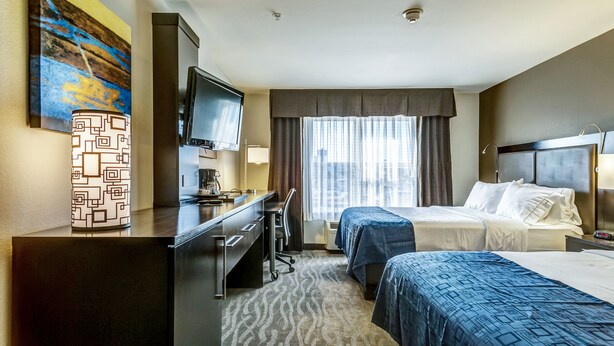Habitación de hotel con dos camas, un escritorio con silla, televisor y ventana con cortinas.
