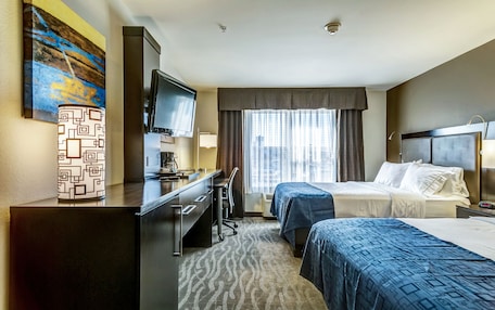 A hotel room with two beds, a desk with a chair, a television, and a window with curtains.