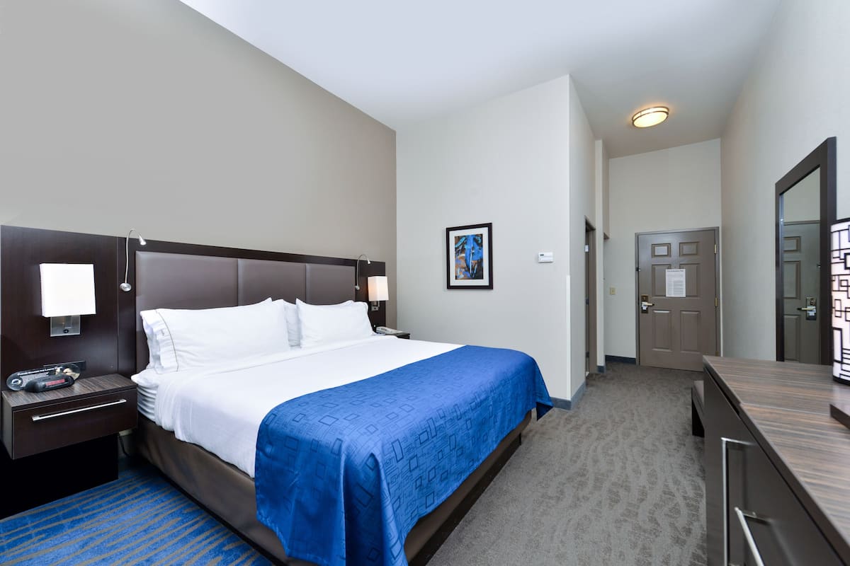 A hotel room with a large bed, a nightstand, a desk, and a door leading to another room.