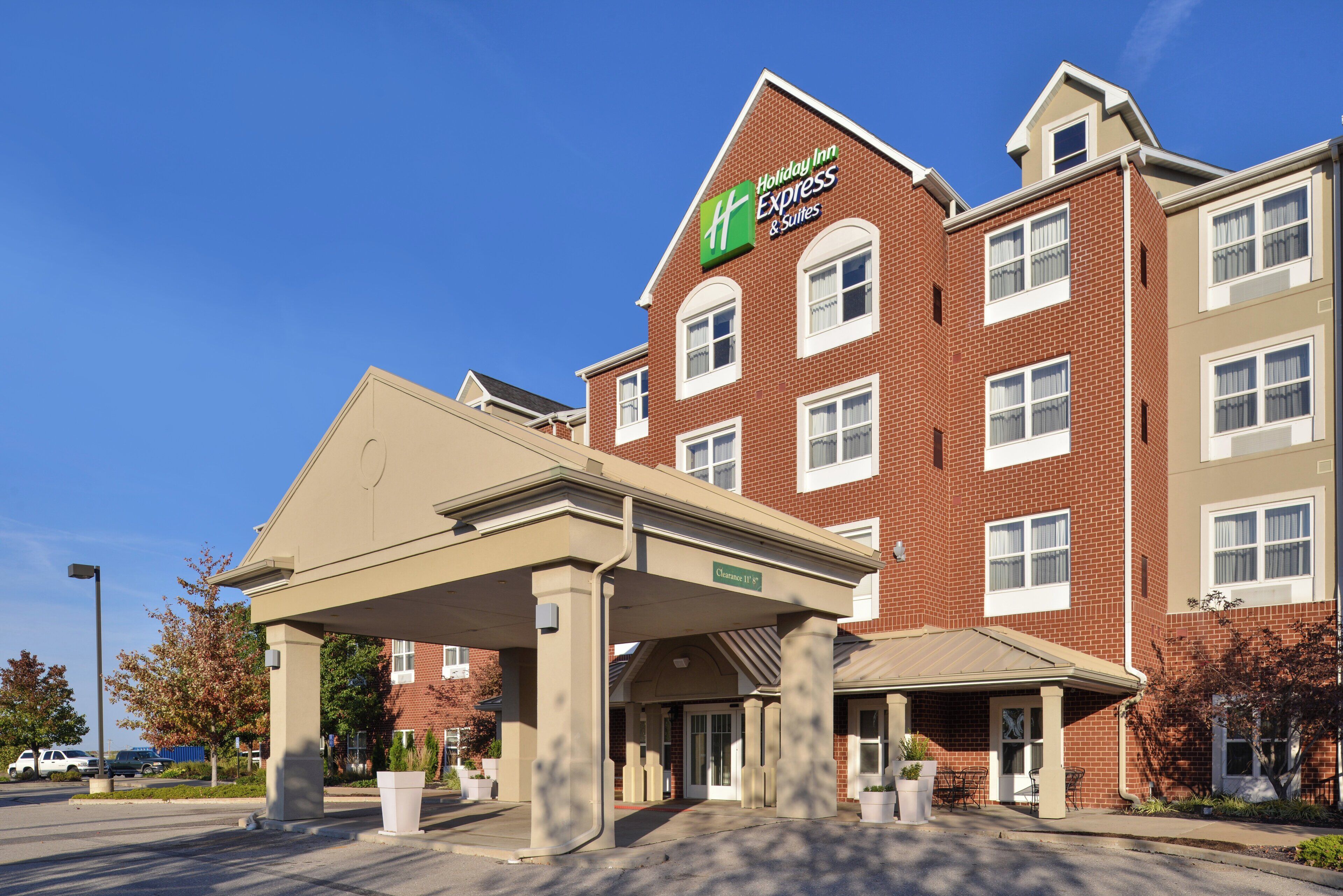 A Holiday Inn Express & Suites with a brick facade, a covered entrance, and a clear sky.