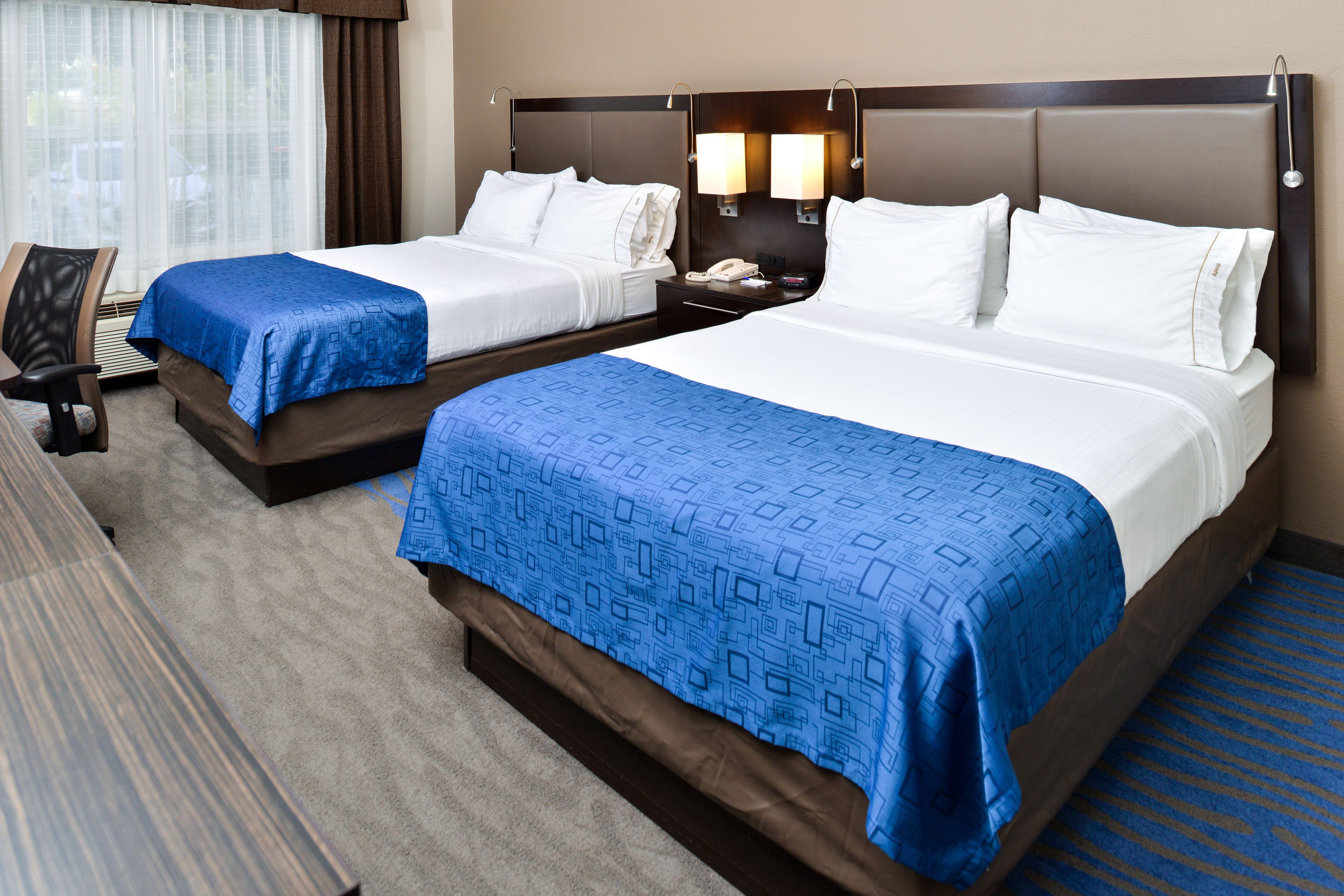 A hotel room with two beds, a desk, and a chair.