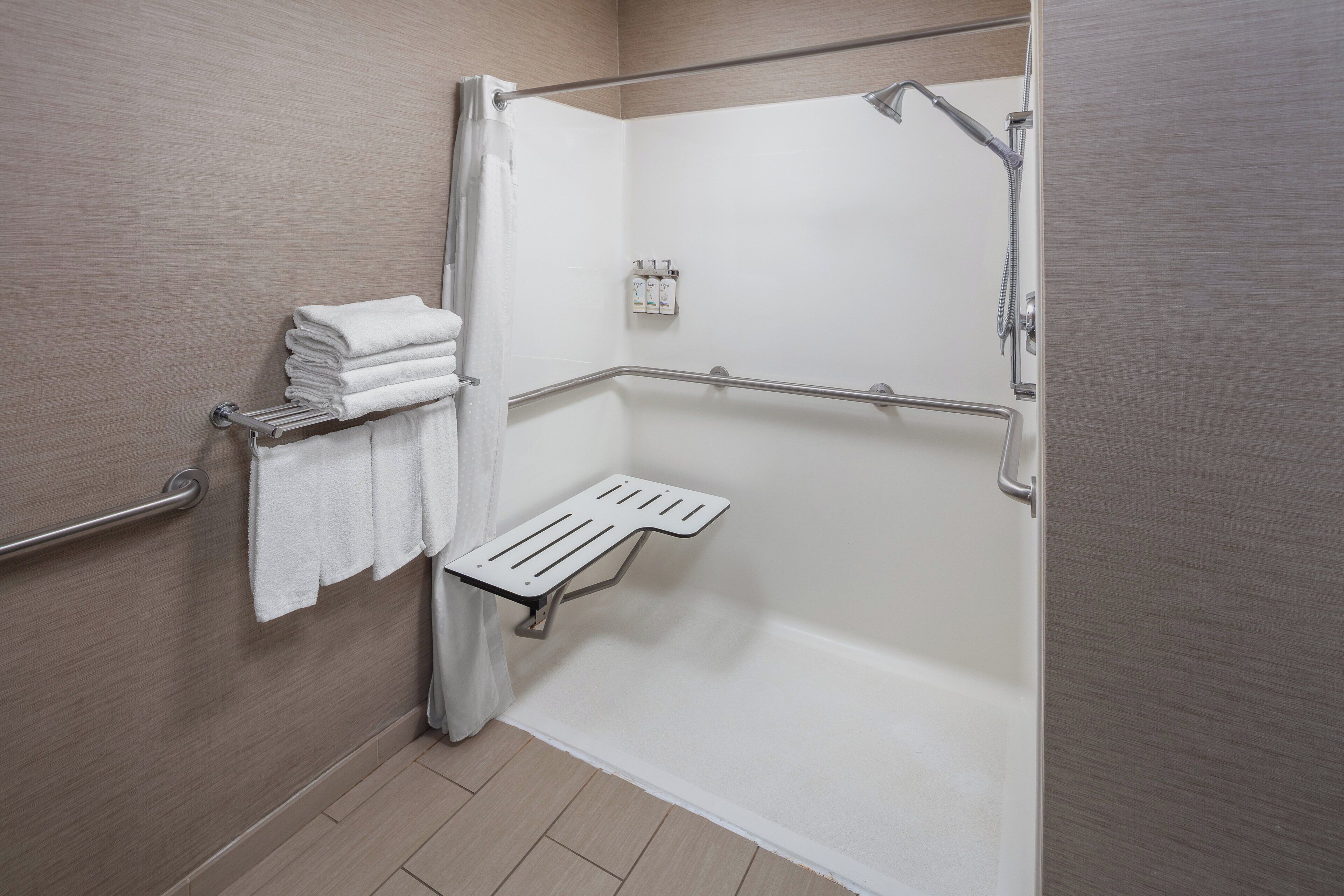 Ein modernes Badezimmer mit barrierefreier Dusche, Haltegriffen, einem Handtuchhalter und einer kleinen Ablagefläche.
