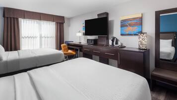 A hotel room with two beds, a desk, a chair, a television, a coffee maker, and artwork on the walls.