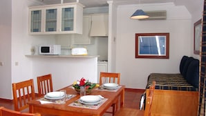 Un coin repas avec une table en bois dressée pour quatre personnes, un four à micro-ondes et une petite cuisine en arrière-plan.
