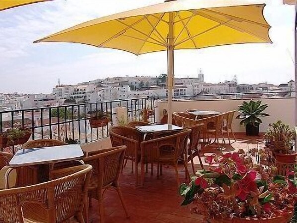 Eine Terrasse mit Korbmöbeln, einem gelben Sonnenschirm und Blumentöpfen.