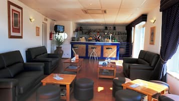 Hall d'hotel con divani in pelle nera, tavoli in legno e un'area bar con un barista.