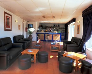 Eine Hotelhalle mit schwarzen Ledersofas, Holztischen und einer Bar, an der ein Barkeeper steht.