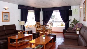 Un hall d’hôtel avec des canapés en cuir marron, des tables en bois et un coin repas doté de chaises en osier.