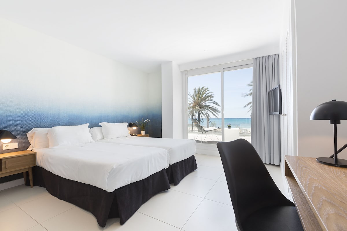 Ein Hotelzimmer mit Bett, Schreibtisch, Stuhl, Fernseher und Blick auf den Strand.