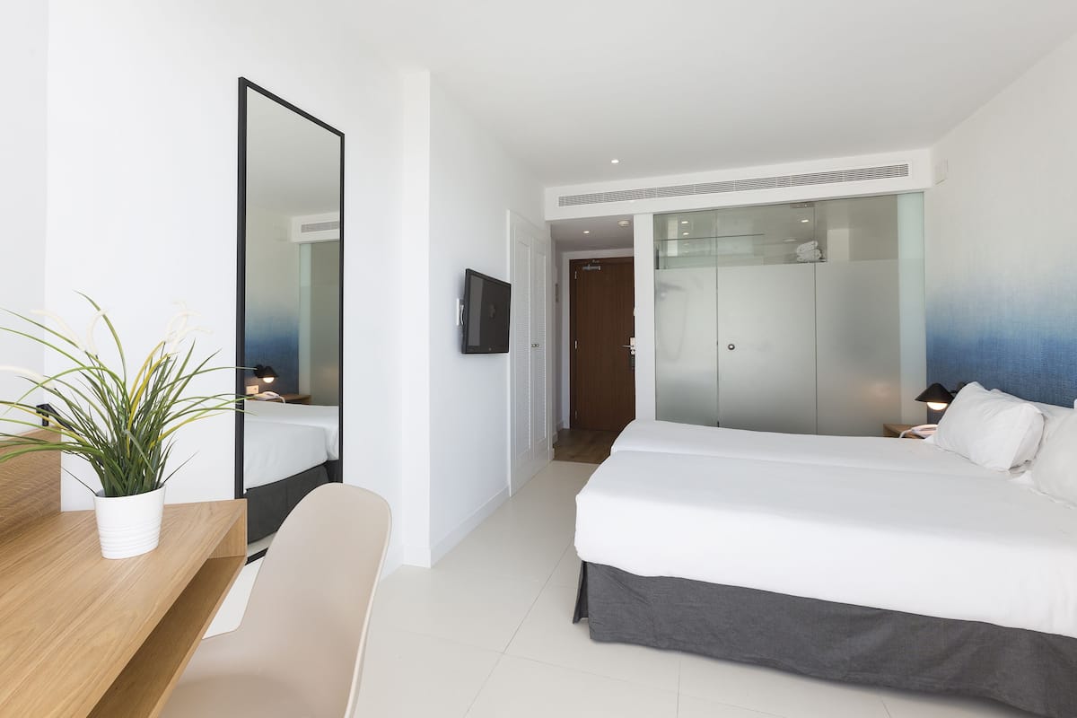 Ein modernes Hotelzimmer mit einem Bett, einem Schreibtisch, einem Stuhl, einem Spiegel und einem Fernseher.