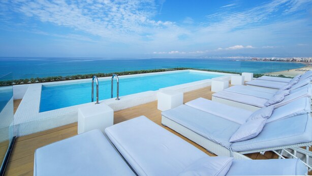 A poolside area with lounge chairs and a view of the sea. - HM Tropical Hotel (Palma de Mallorca)