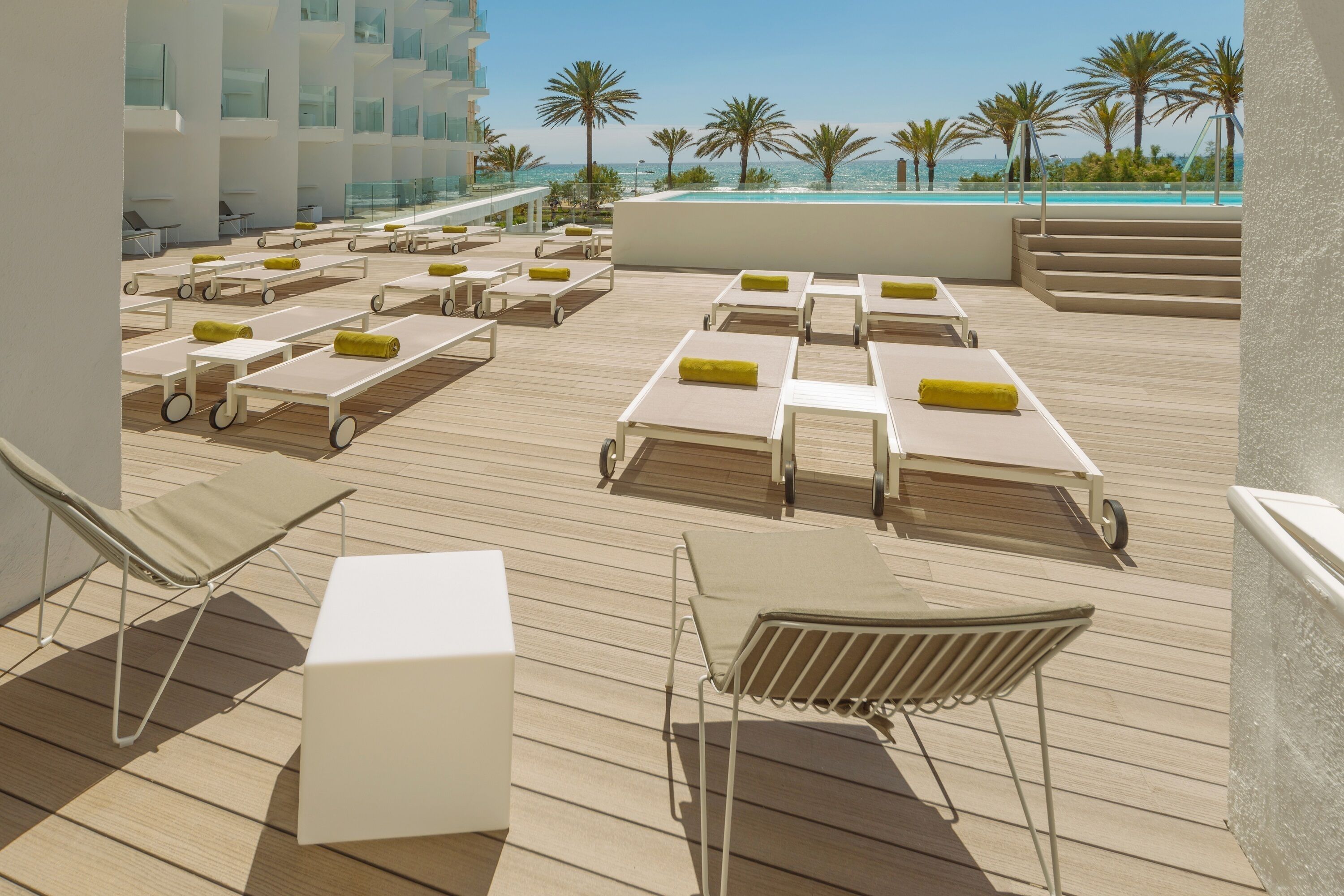 Solterrasse med liggestole og swimmingpool med udsigt over en strand med palmer.
