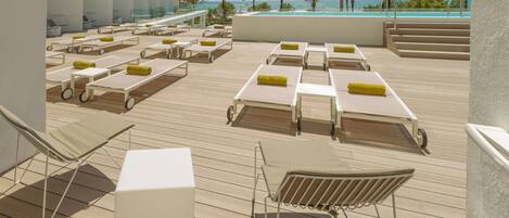 Solterrasse med liggestole og swimmingpool med udsigt over en strand med palmer.