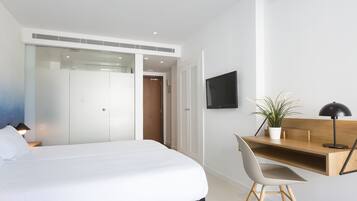 A modern bedroom with a bed, a desk, a chair, a TV, and a potted plant.