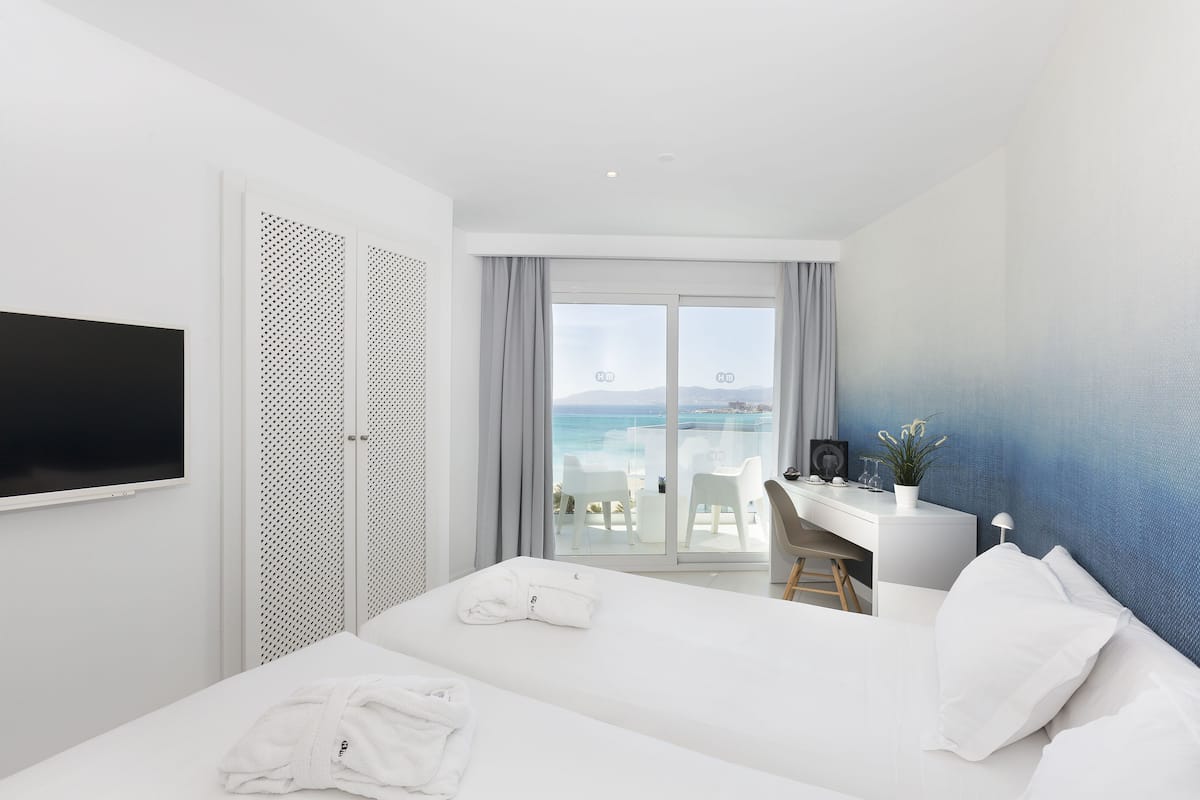 Ein Hotelzimmer mit Bett, Schreibtisch, Stuhl, Fernseher und einem Balkon mit Meerblick.
