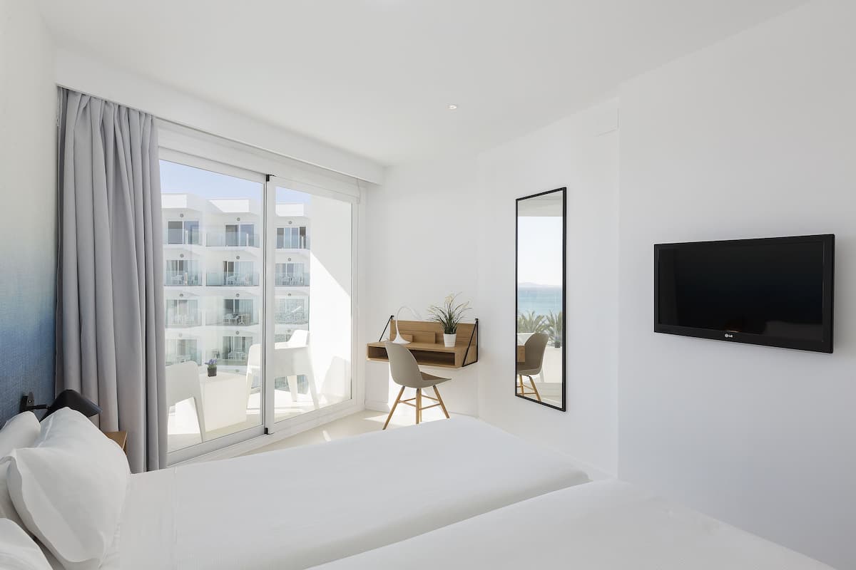 Ein modernes Hotelzimmer mit einem großen Bett, einem Schreibtisch mit Stuhl, einem Flachbildfernseher und einem Balkon mit Blick auf die Stadt.