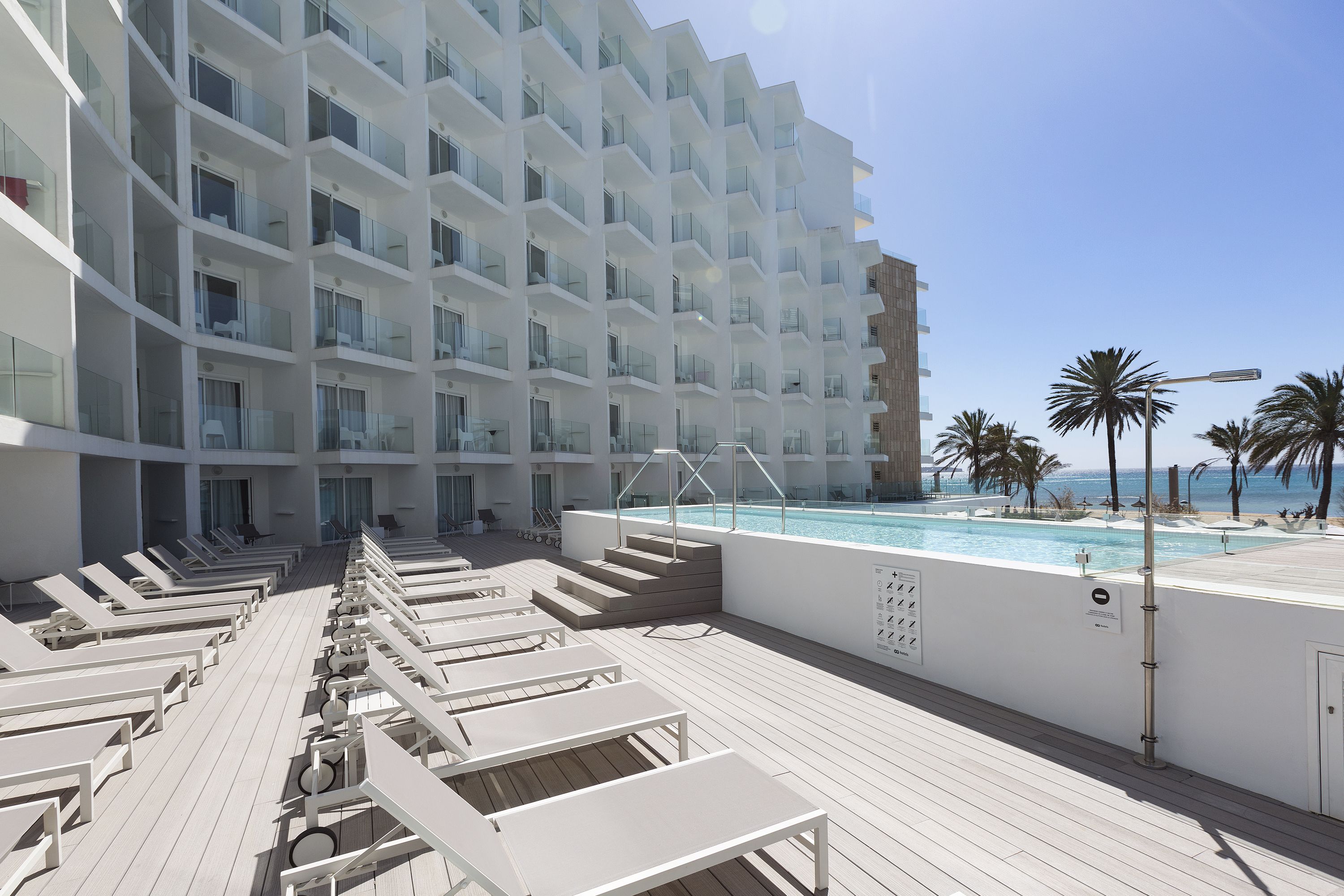 A modern hotel with a pool area, sun loungers, and a view of the ocean.