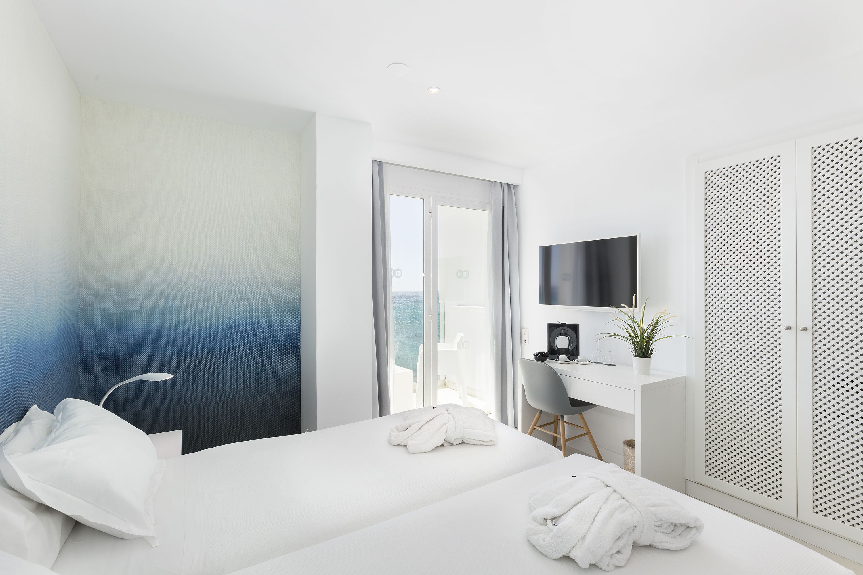 Una habitación de hotel moderna con una cama, un escritorio, un televisor y un balcón con vistas.
