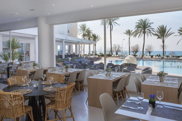 A restaurant with outdoor seating overlooking a pool and palm trees, featuring wicker chairs and tables set for dining. - HM Tropical Hotel (Palma de Mallorca)