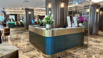 A modern hotel lobby with a reception desk, seating area, and a view of the bar and dining area.