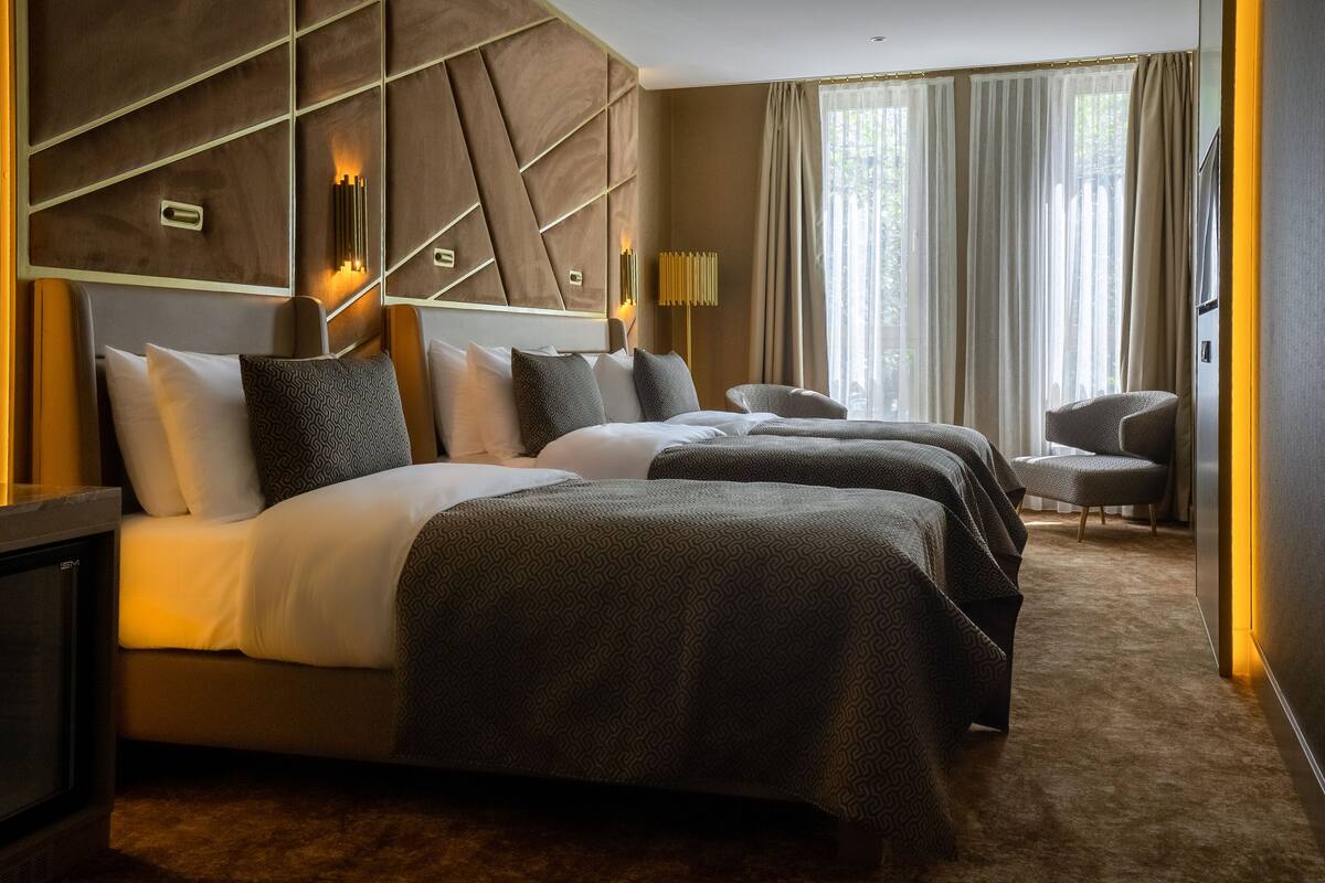 A hotel room with two beds, a seating area, and a large window with curtains.