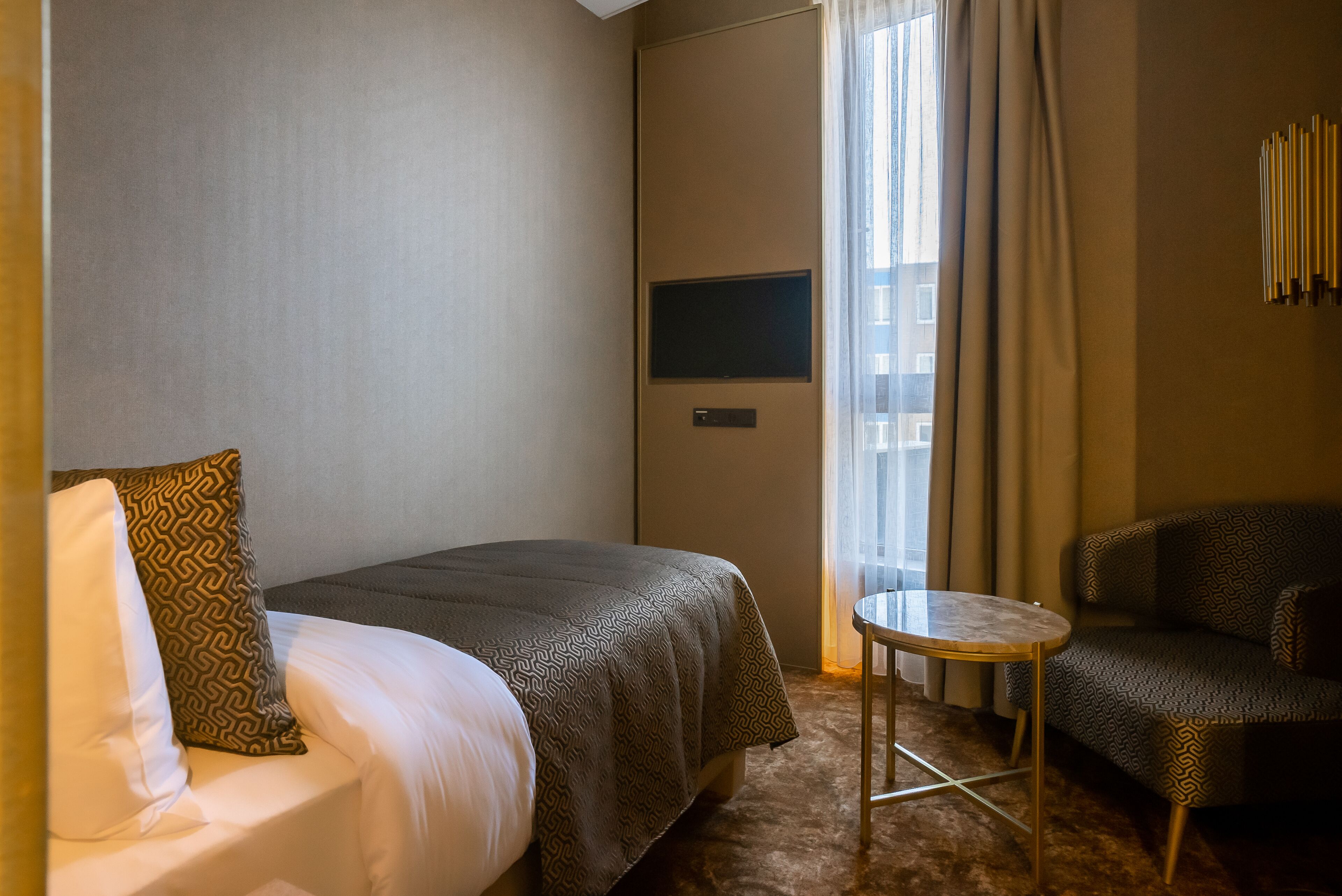 Una camera d'albergo con un letto, un piccolo tavolo rotondo, un divano, una televisione e una finestra con tende.