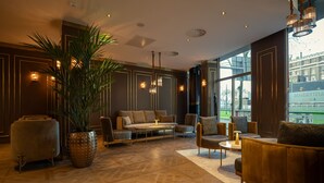 A modern lounge with a sofa, armchairs, and a coffee table. There is a large potted plant and a decorative lamp. - Art Hotel Rotterdam (Rotterdam)