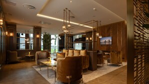 A modern hotel lobby with a sofa set, a TV mounted on the wall, and a large window offering a view of the city. - Art Hotel Rotterdam (Rotterdam)