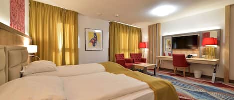 A hotel room with a bed, two red chairs, a desk with a TV, and a large window with yellow curtains.