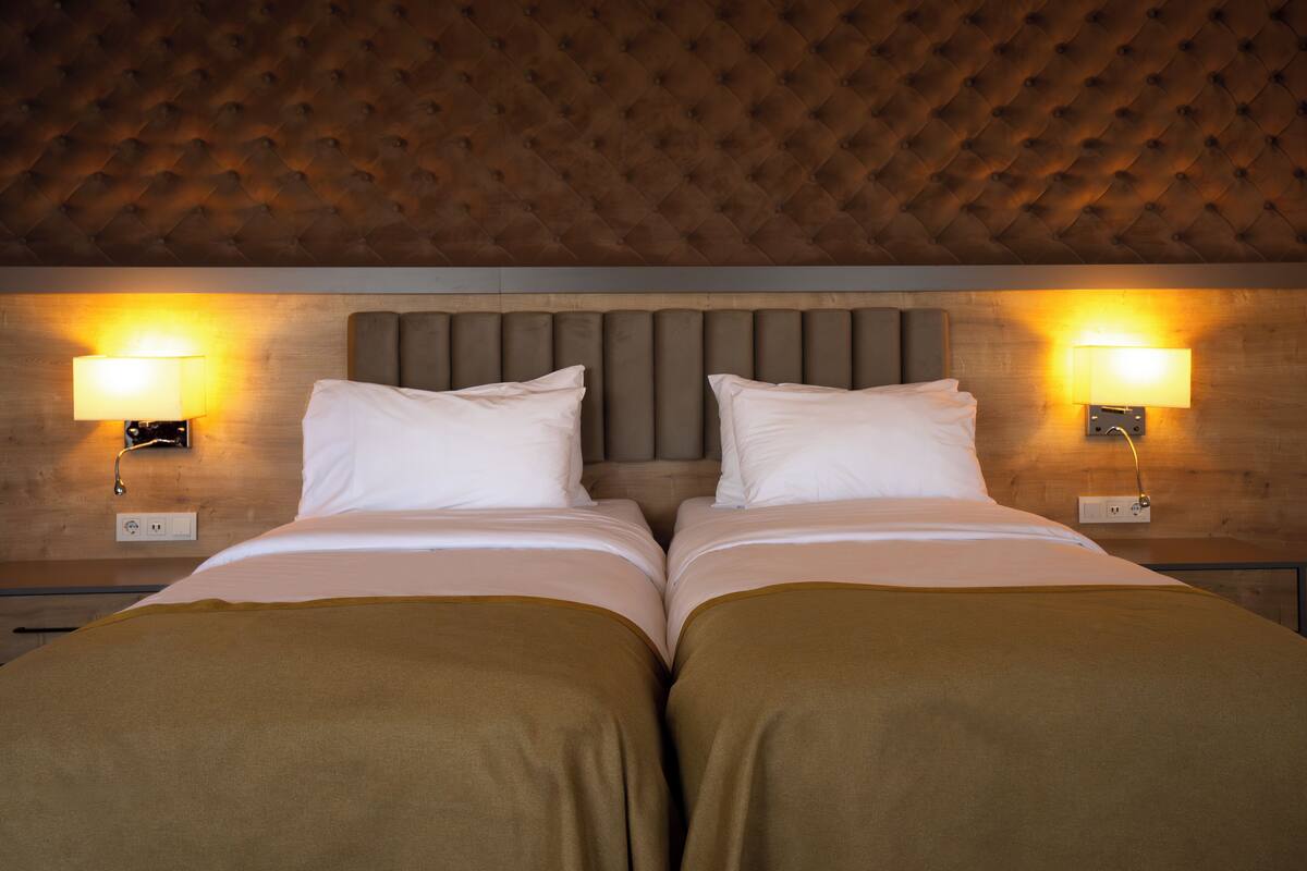 A double bed with a tufted headboard, two bedside lamps, and a wooden wall panel.