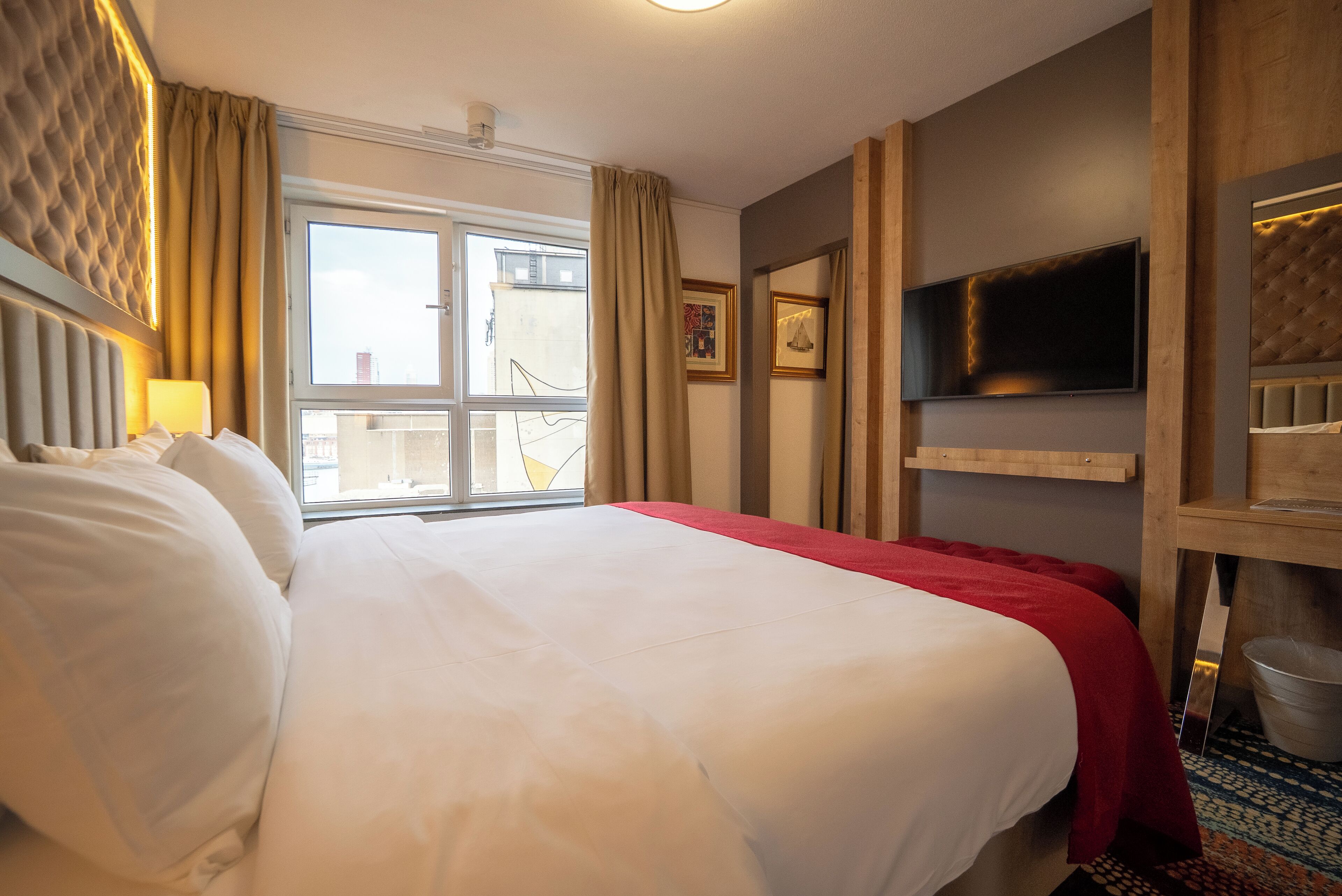 Habitación de hotel con una cama grande, un televisor montado en la pared y una ventana con cortinas.